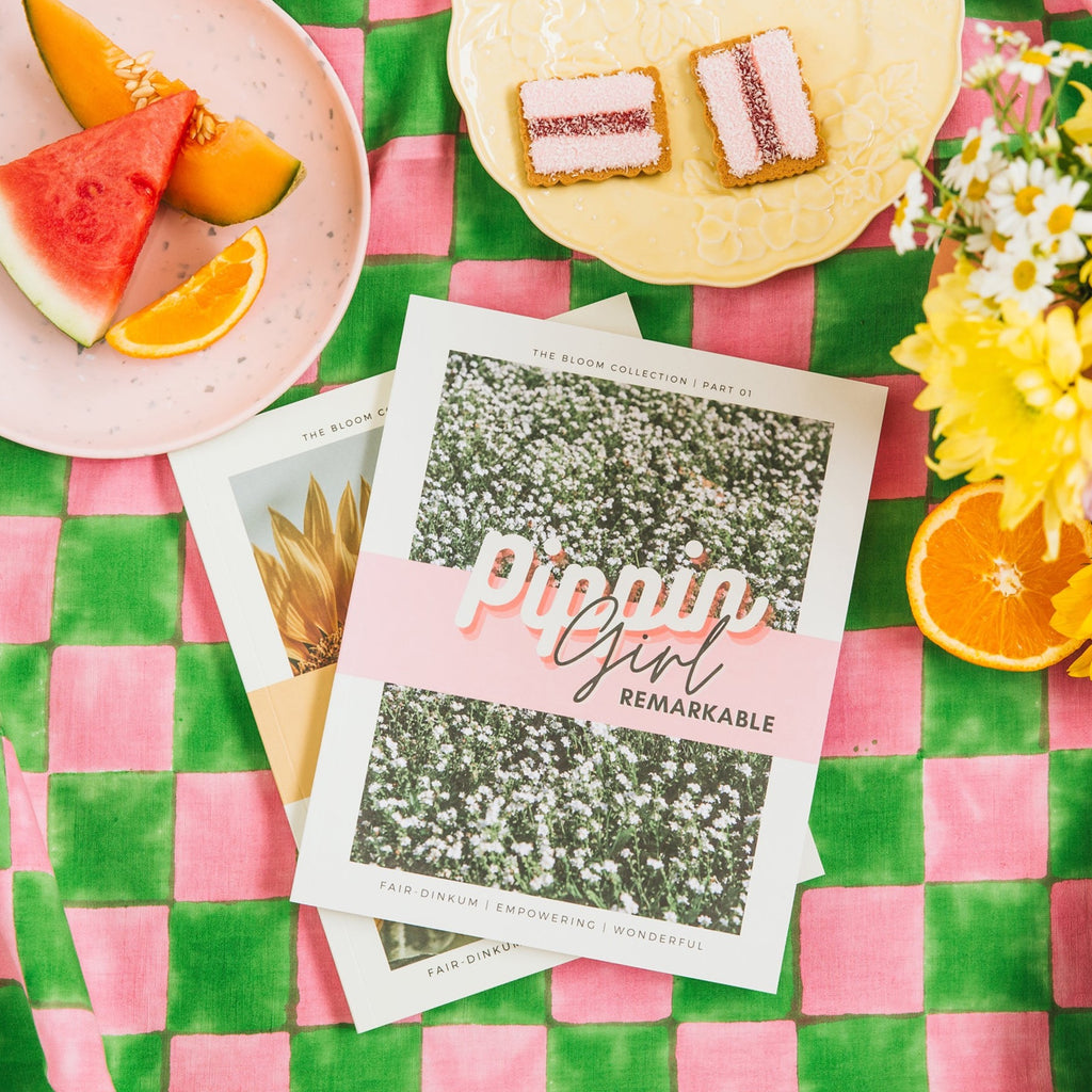 pippin girl bloom books 01  and 02 on a bright pink and green check tablecloth with fruit, iced vo vos and flowers in the background.