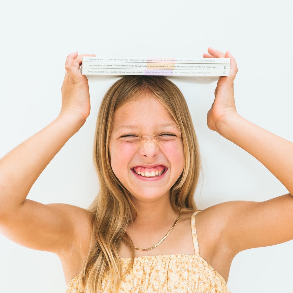 Happy girl holding a stack of Pippin Girl Bloom collection books cheekily on her head