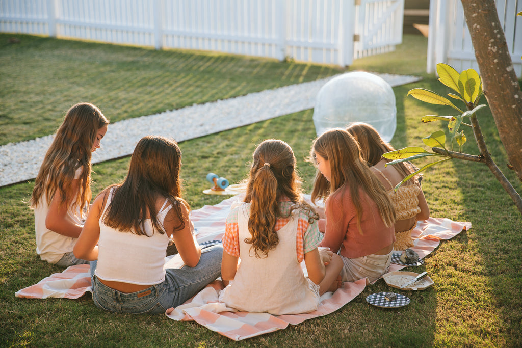 Back view of five girls sitting on picnic rug in the front garden enjoying each other's friendship