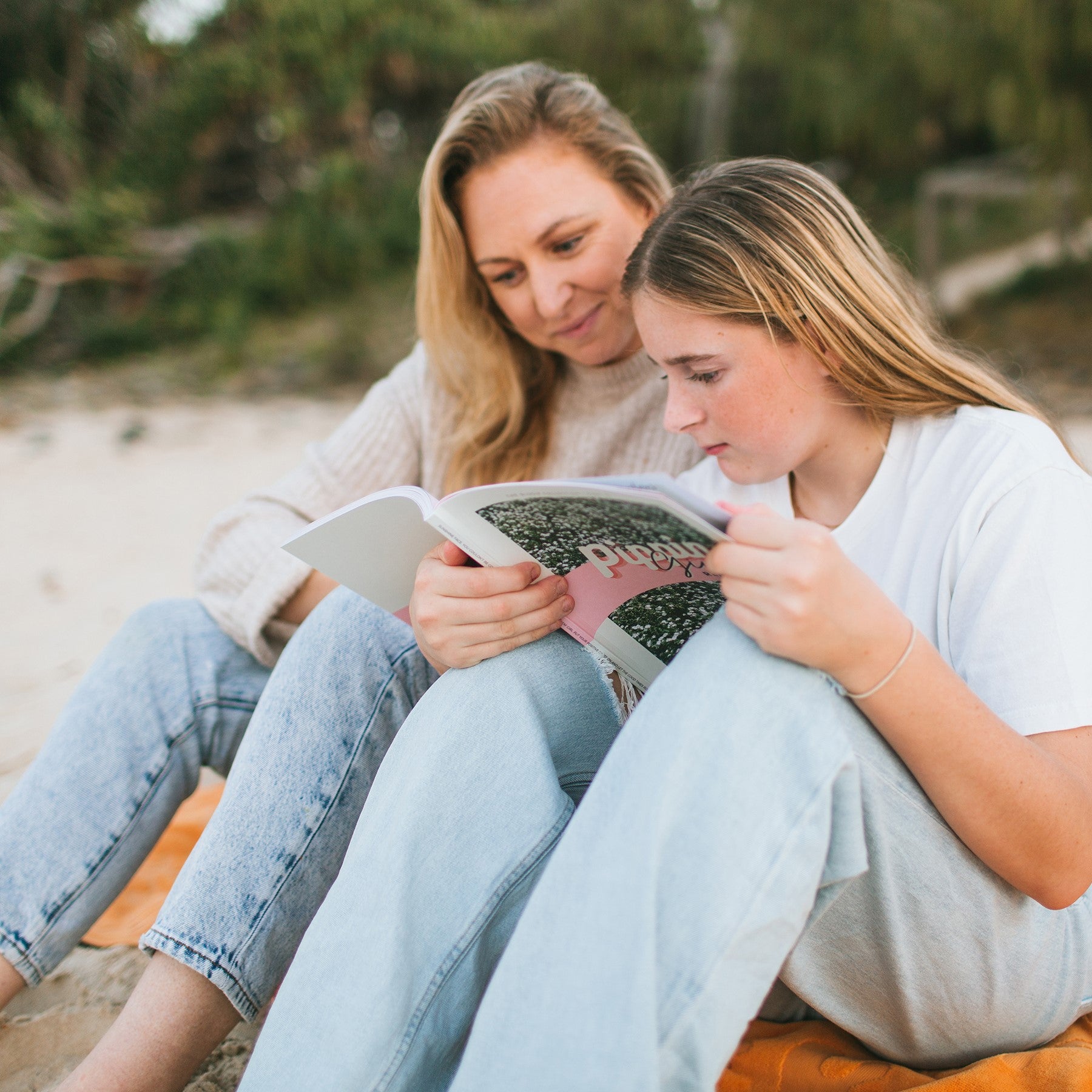 mother and daugher sittiing on an orange towel at the beach discussing puberty and reading Pippin Girl Remarkable book together