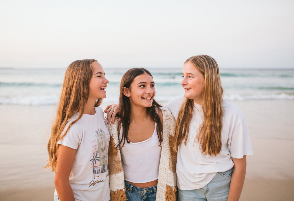 Three friends (girls) at the beach. The headland is in the background.