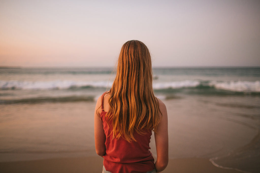 Back view of girl looking at the ocean at sunset. She is wearing a red singlet.