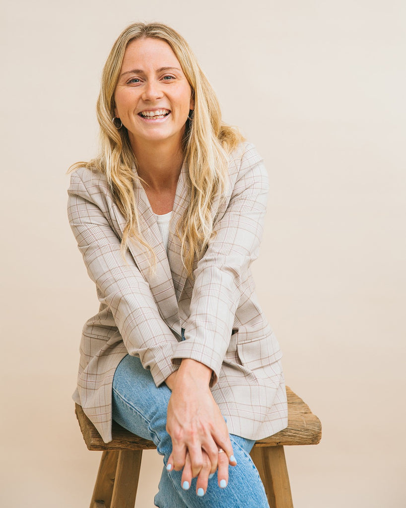 Pippin Girl founder Emma Tabacaru sitting on wooden stool wearing casual blazer and jeans.
