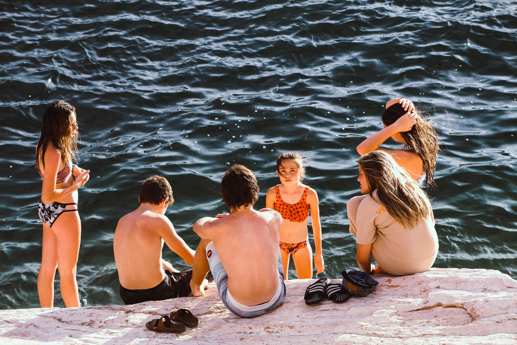 a mixed friendsip group of boys and girls sitting on a boulder at the ocean